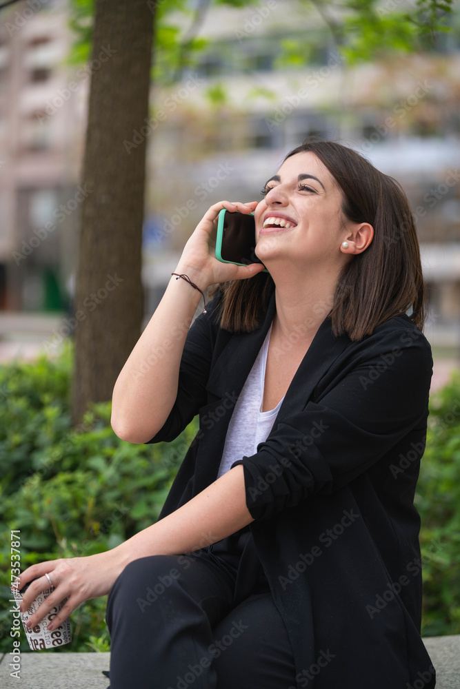 Happy young woman talking on mobile phone while sitting at park Happy young woman talking on mobile phone while sitting at park