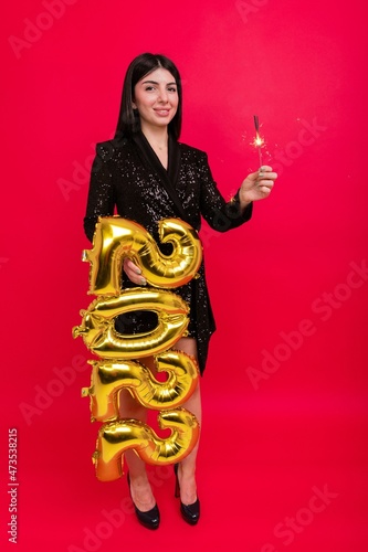 Christmas, the concept of holidays - A young woman in a shiny dress holds the numbers 2022 and a sparkler