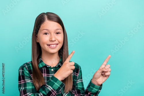 Photo of dreamy charming schoolgirl wear plaid outfit looking pointing two fingers empty space smiling isolated turquoise color background