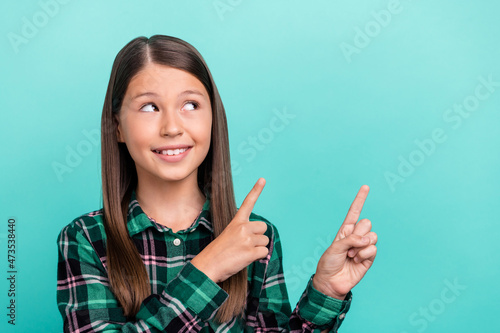 Photo of sweet adorable school girl dressed checkered clothes pointing two fingers looking empty space isolated teal color background
