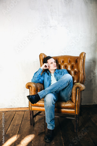 Portrait of Young stylish man in denim or jeans clothes who seat on the armchair in photo studio. © Vadym