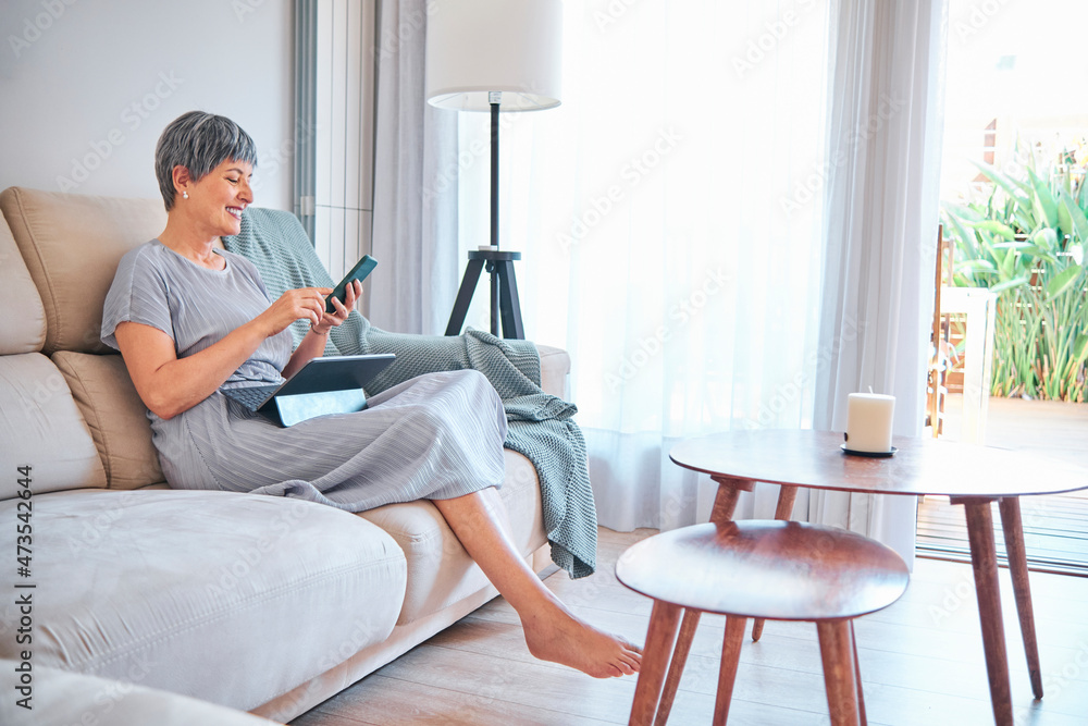 Woman using smart phone while sitting on sofa in living room at home Woman using smart phone while sitting on sofa in living room at home