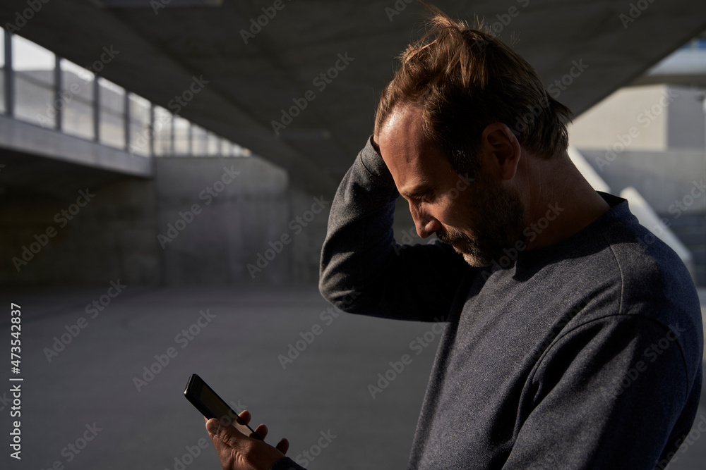 Mature businessman with hand in hair using mobile phone while standing under bridge Mature businessman with hand in hair using mobile phone while standing under bridge