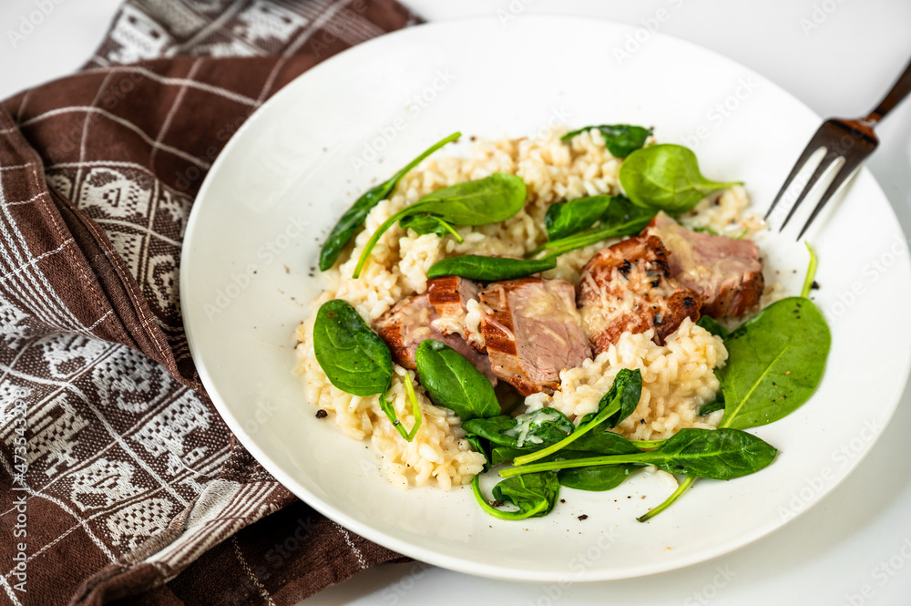 Pork tenderloin medallions on risotto with parmesan and spinach leaf on white plate and towel. Pork tenderloin medallions on risotto with parmesan and spinach leaf on white plate and towel.