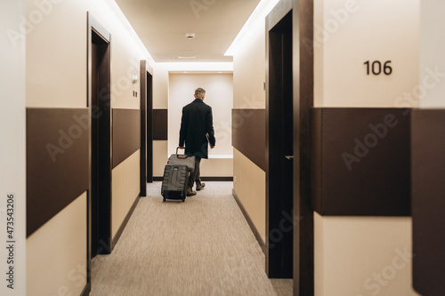 Businessman walking with briefcase and luggage at hotel corridor photo