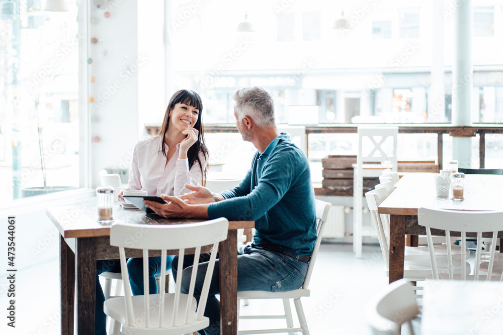 Businessman with digital tablet explaining to colleague while sitting at cafe Businessman with digital tablet explaining to colleague while sitting at cafe