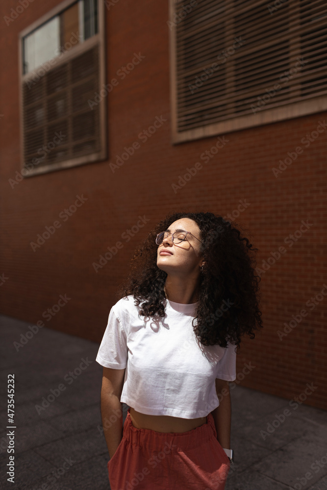 Young woman with hands in pockets in front of building during sunny day Young woman with hands in pockets in front of building during sunny day