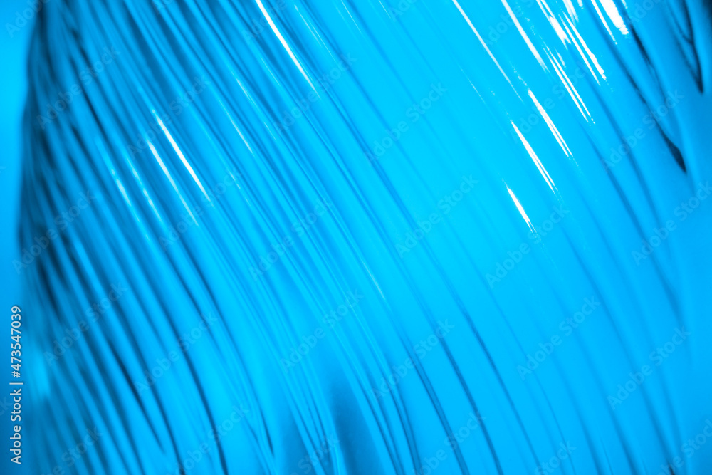 Ribbed glass with wavy pattern illuminated in blue light. Creating volume with light. Abstract background with copy space. Ribbed glass with wavy pattern illuminated in blue light. Creating volume with light. Abstract background with copy space.