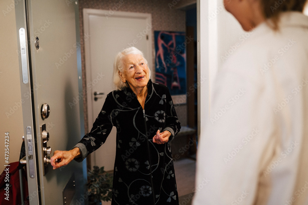 Smiling senior woman opening door while female nurse arriving at home Smiling senior woman opening door while female nurse arriving at home