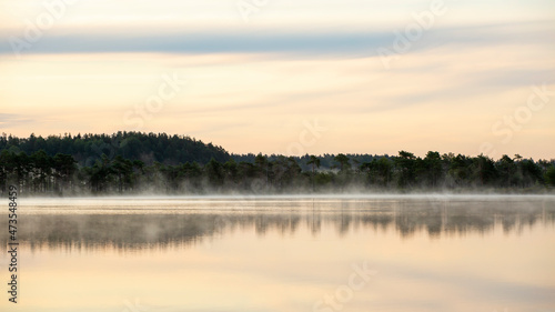 Fog rising slowly on the lake during early morning sunrise at Kakerdaja bog in Estonia, Northern Europe