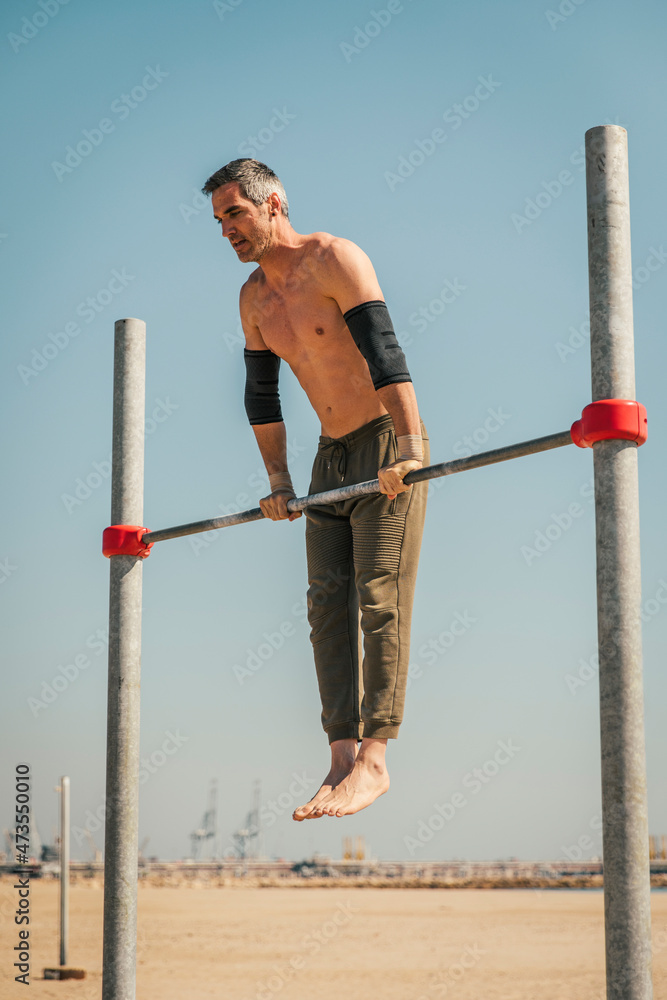 Male sportsperson exercising on high bar during sunny day Male sportsperson exercising on high bar during sunny day