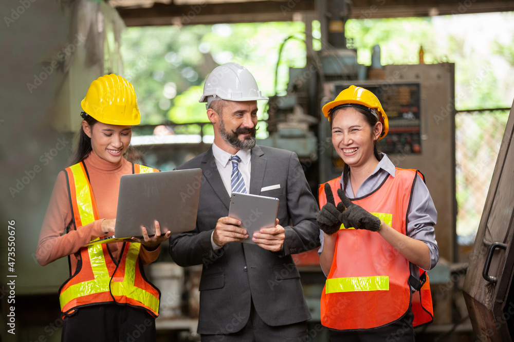 Male engineer and Industrial workers in Hard Hats Discuss New Project while Using Laptop. They Make Showing Gestures.They Work in a Heavy Industry Manufacturing Factory. Male engineer and Industrial workers in Hard Hats Discuss New Project while Using Laptop. They Make Showing Gestures.They Work in a Heavy Industry Manufacturing Factory.