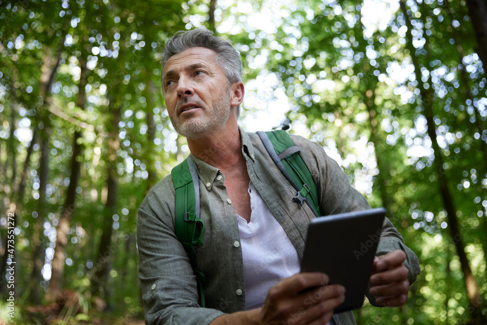 Thoughtful man with backpack holding digital tablet at forest Thoughtful man with backpack holding digital tablet at forest