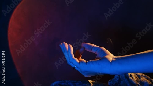 Woman meditating with aroma sticks, colourful artificial light on background. Closeup of female hand in a dzen sign. Meditation for life balance. Harmony and mental health concept. photo