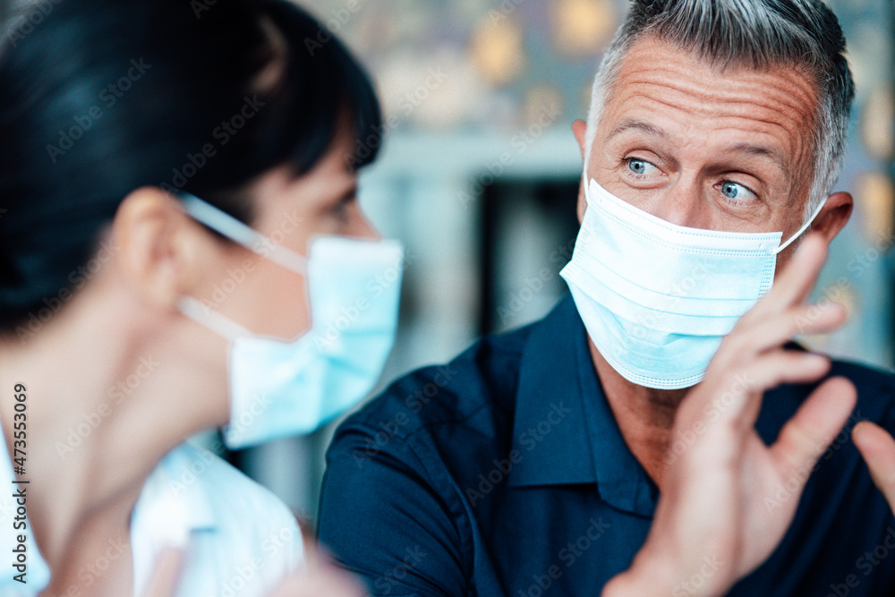 Businessman wearing protective face mask discussing with colleague at cafe Businessman wearing protective face mask discussing with colleague at cafe