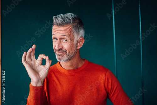 Mature man gesturing OK sign in front of wall photo