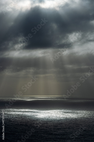 Sunlight through dark rainy clouds at ocean.