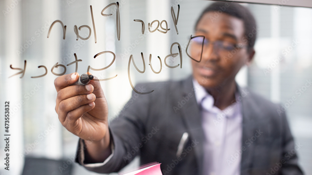 African American young man writing note on a transparent wipe board and thinking of a solution for him work-related problems, Colleagues Having A Business Meeting African American young man writing note on a transparent wipe board and thinking of a solution for him work-related problems, Colleagues Having A Business Meeting
