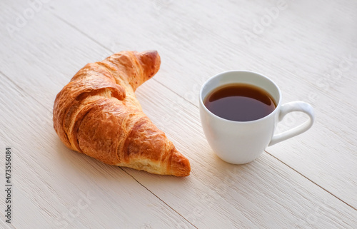 Cup of coffee with croissant on white wooden background