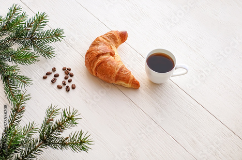 Cup of coffee with croissant, coffee beans and branches of christmas tree on white wooden background