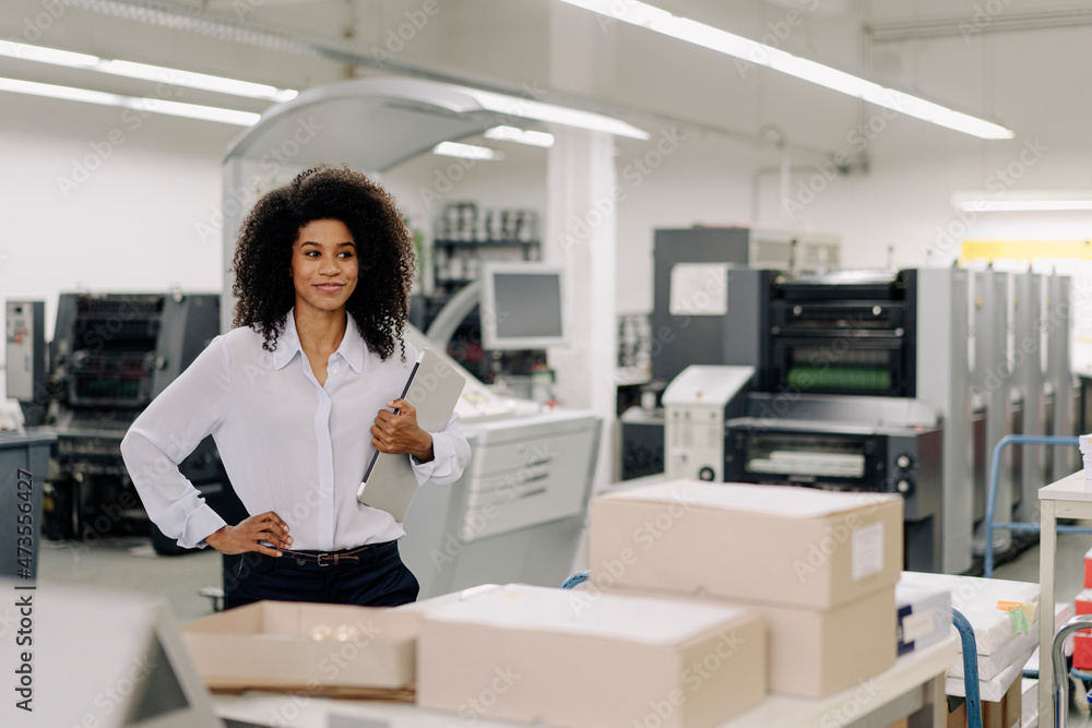 Female professional with hand on hip holding laptop in industry Female professional with hand on hip holding laptop in industry