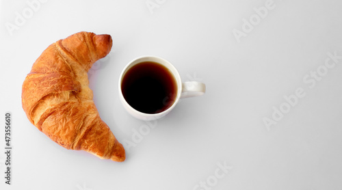 Cup of coffee with croissant on white wooden background