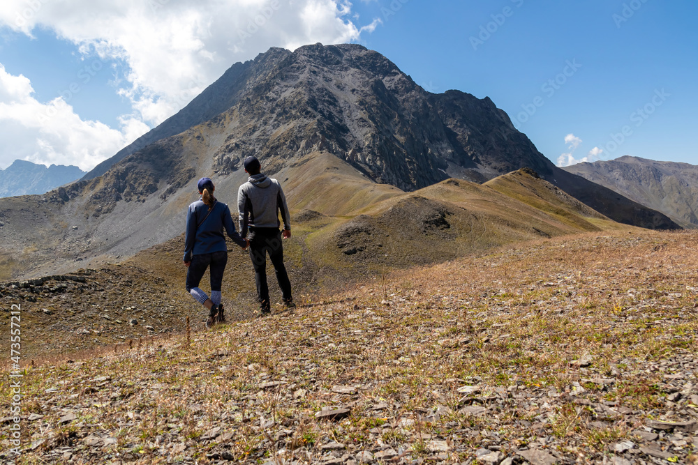 A couple watching the sharp mountain peaks of the Chaukhi massif form the Chaukhi Pass in the Greater Caucasus Mountain Range in Georgia, Kazbegi Region. Hiking together in the Georgian Dolomites.