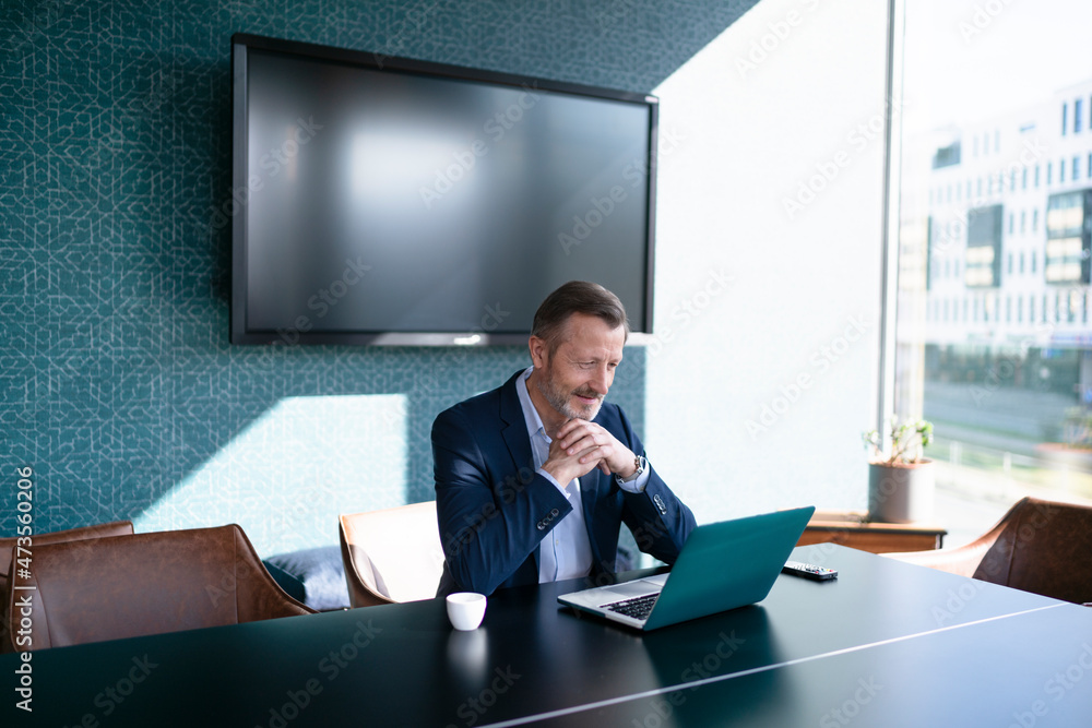 Businessman with hands clasped sitting in front of laptop at table in office Businessman with hands clasped sitting in front of laptop at table in office