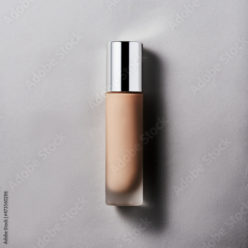 Foundation colored cream in glasse tube with chrome cap on gray backdrop