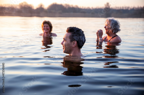 Smiling man looking away while female friends with hands clasped enjoying cold water during morning