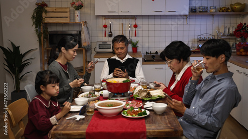 asian family with mixed generation playing with mobile phones and ignoring each other while having reunion dinner at table on chinese new year's eve at home