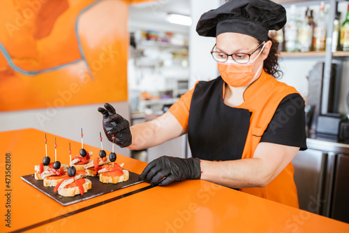 Female chef putting toothpicks in sandwich at cafeteria during COVID-19 photo