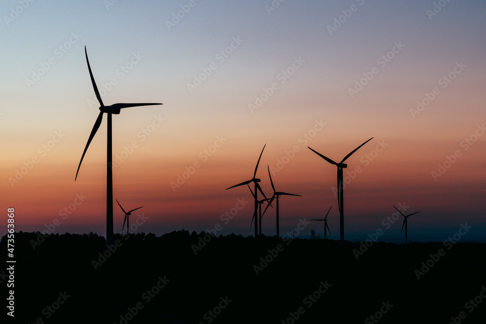 Silhouettes of wind turbines standing against moody sky at dusk