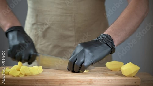 Close-up of men's hands in black disposable gloves. The cook is slicing potatoes on a cutting board.