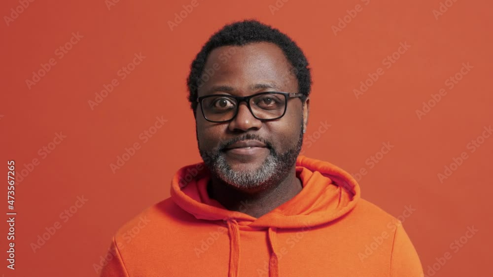 Smiling mature African man looking around and showing silence gesture in the orange studio Smiling mature African man looking around and showing silence gesture in the orange studio