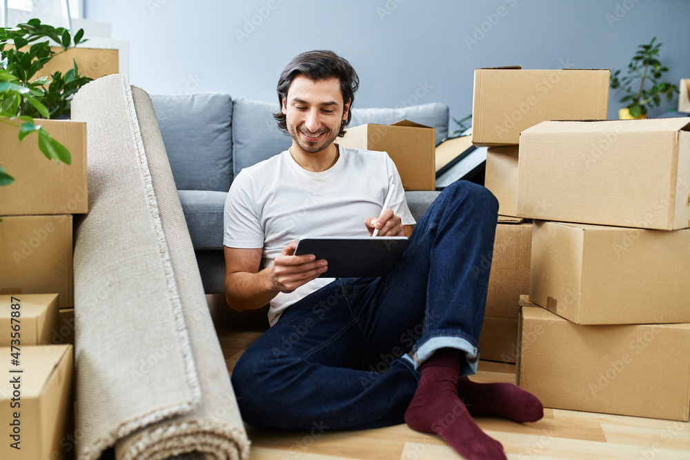 Man using graphic tablet amidst cardboard boxes at home Man using graphic tablet amidst cardboard boxes at home