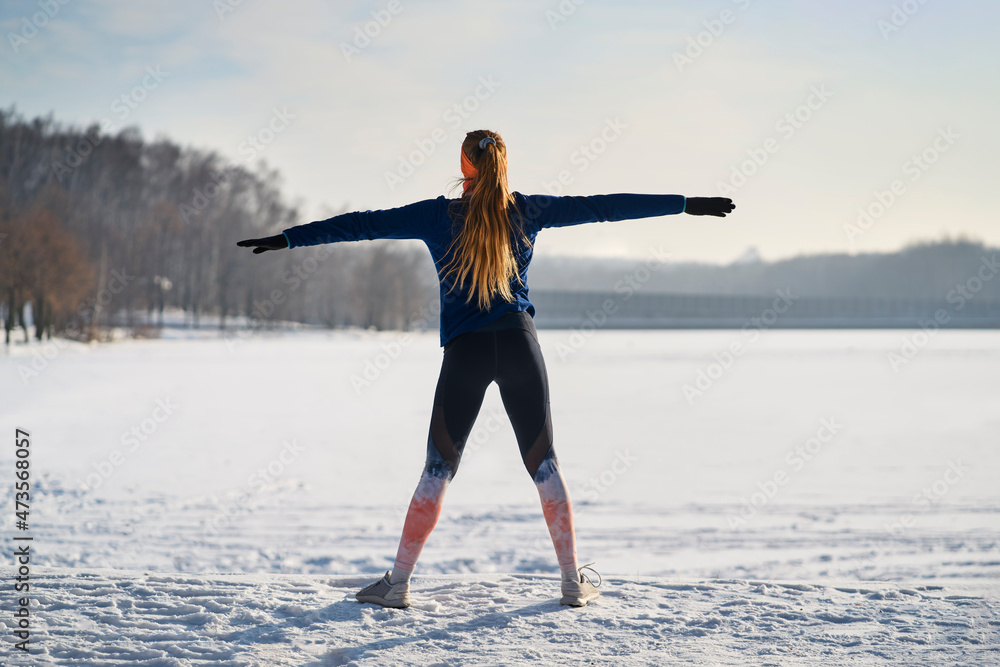 Woman exercising with arms outstretched on snow during winter