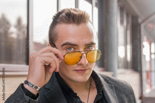 Portrait of a handsome man of European appearance businessman adjusting sunglasses with his hand, close-up on the outdoor of the street