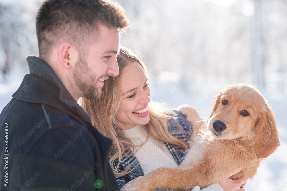 Smiling couple looking at dog during winter Smiling couple looking at dog during winter