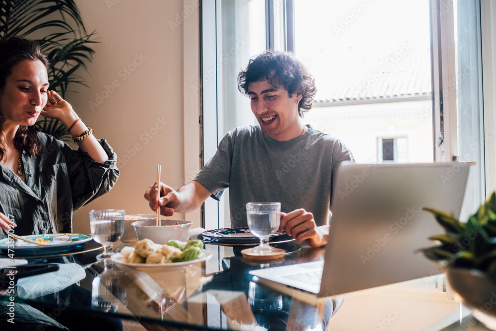 Smiling man eating food while sitting by woman at home Smiling man eating food while sitting by woman at home