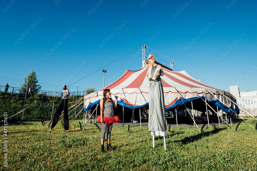 Female acrobat looking at performer playing accordion while standing with stilts on meadow Female acrobat looking at performer playing accordion while standing with stilts on meadow