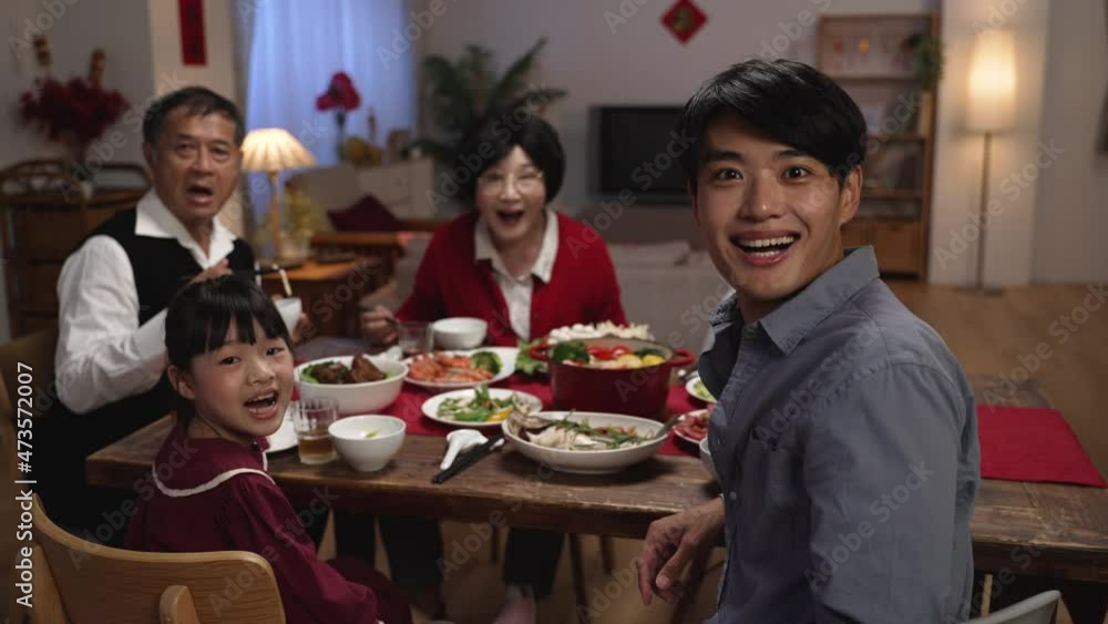 rear view surprised asian father and daughter turning to look at camera with other family members, showing wonder as someone walking near dinner table with delicious food. text translation: fortune rear view surprised asian father and daughter turning to look at camera with other family members, showing wonder as someone walking near dinner table with delicious food. text translation: fortune