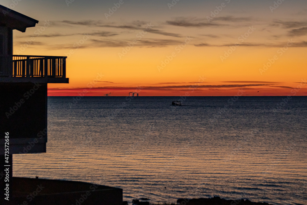 An orange sunrise over the ocean with the silhouette of a resort with a balcony.