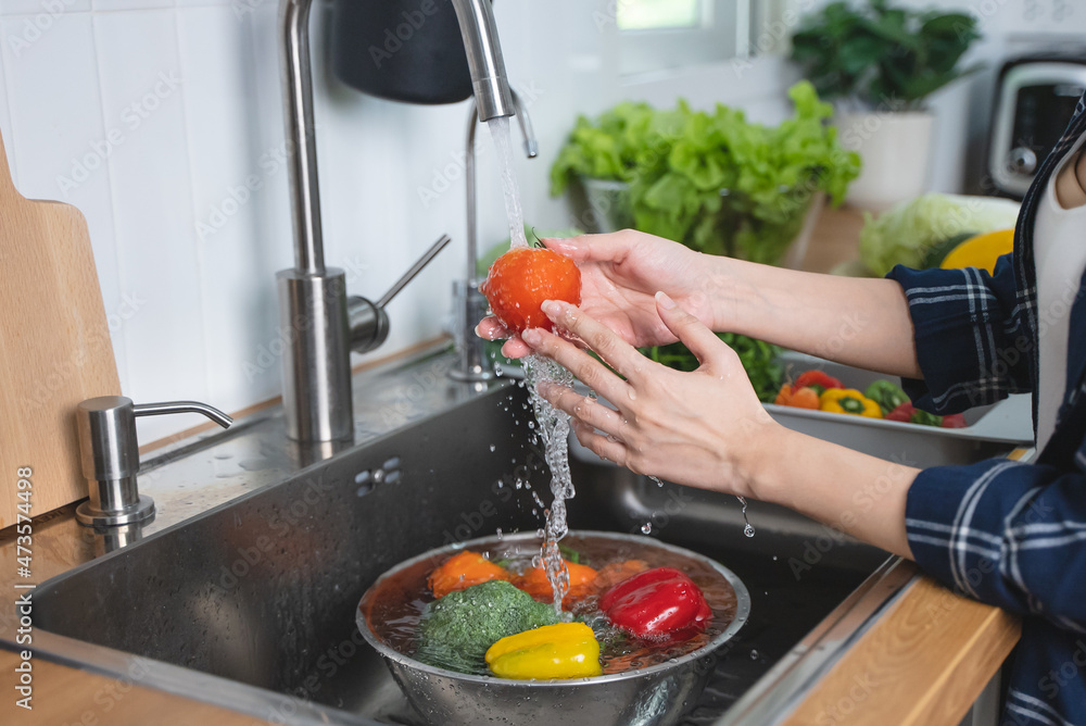 Close up of hands people washing vegetables by tap water at the sink in the kitchen to clean ingredient prepare a fresh salad.