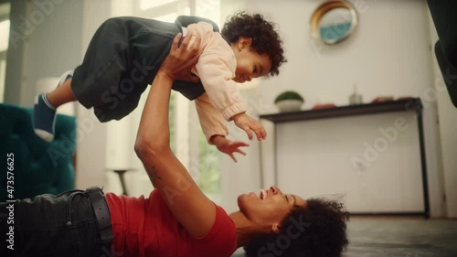 Beautiful Black Latina Mother Playing with Adorable Baby Boy at Home on Living Room Floor. Cheerful Mom Nurturing a Child. Happy Son Raised in the Air. Concept of Childhood, New Life, Parenthood. photo