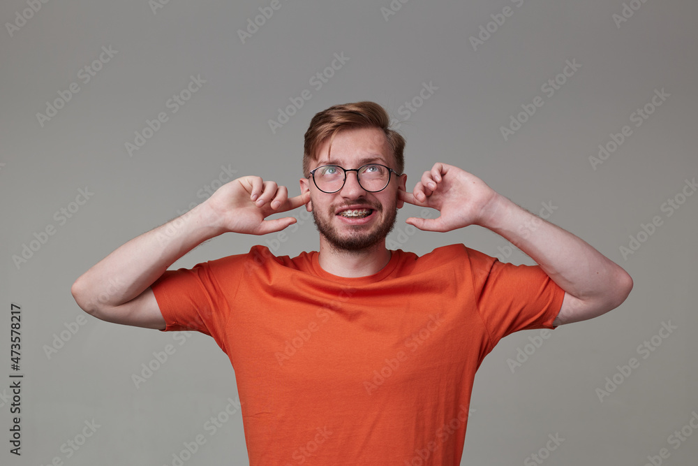 Studio portrait of young bearded man, wears casually posing over gray studio background plug his ears with a fingers, looks upwards feels angry isolated. Studio portrait of young bearded man, wears casually posing over gray studio background plug his ears with a fingers, looks upwards feels angry isolated.