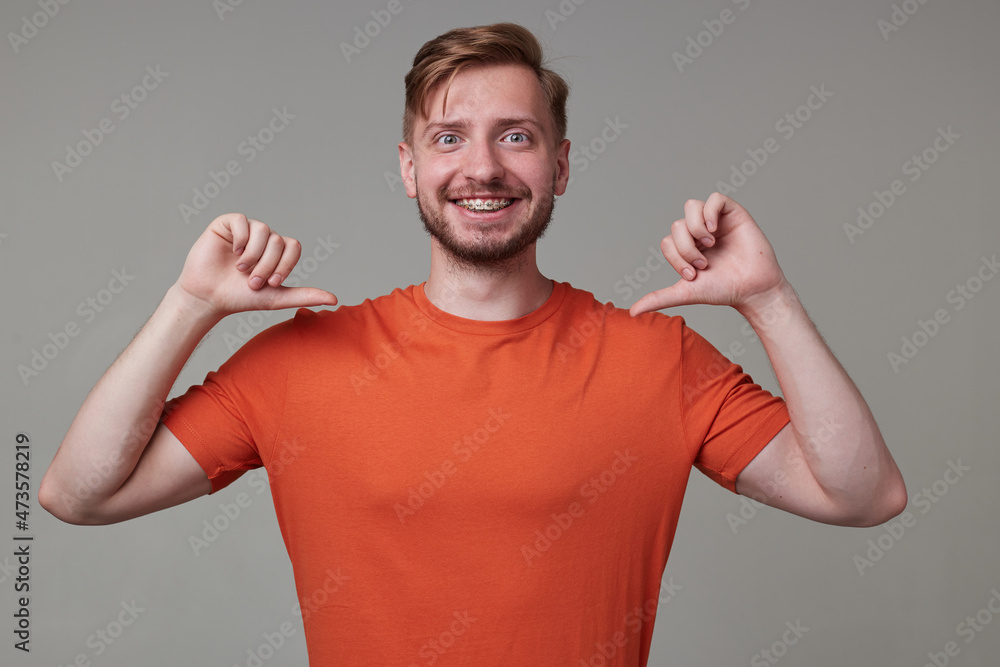 Studio portrait of young bearded man, wears casually posing over gray studio background points with a finger at himself, smiles broadly with happy facial expression. isolated. Studio portrait of young bearded man, wears casually posing over gray studio background points with a finger at himself, smiles broadly with happy facial expression. isolated.