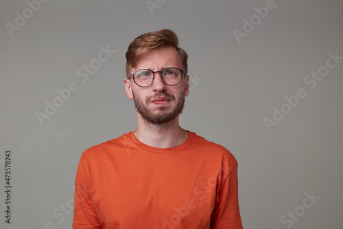 Studio portrait of young bearded man, wears casually posing over gray studio background curves his lips while thinking about future. isolated. © timtimphoto