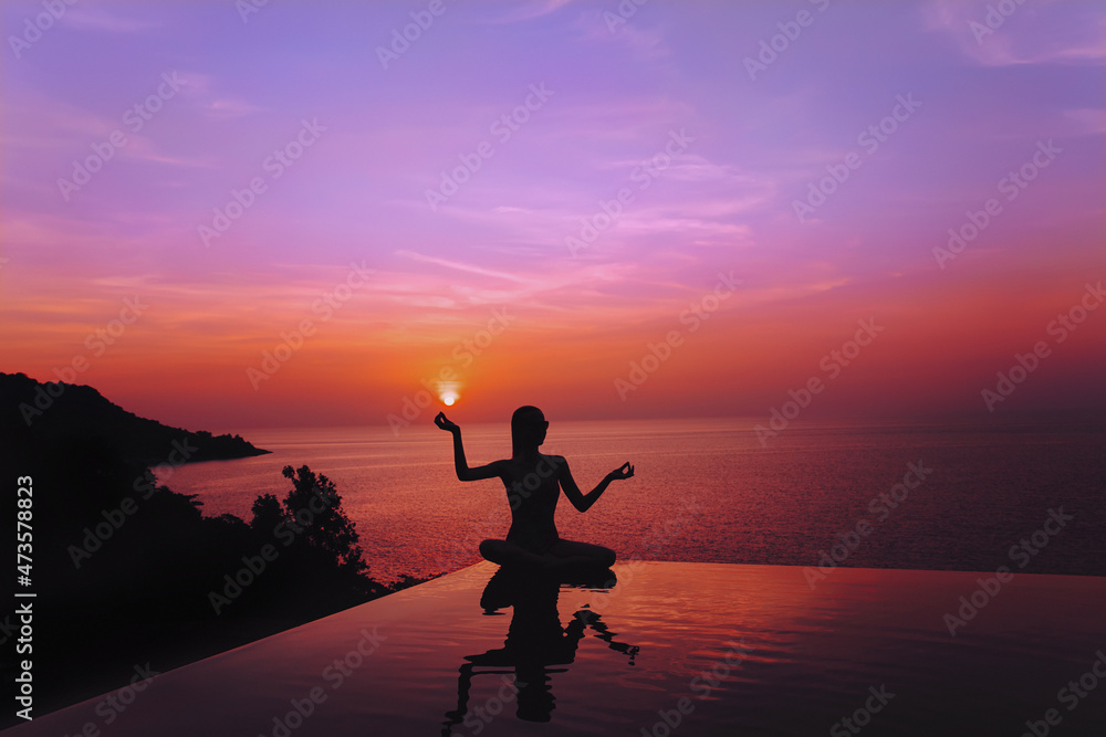 A silhouette of a girl sitting on the edge of the swimming pool overlooking amazingly beautiful sunset.