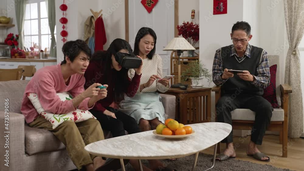 asian family ignoring each other while spending time on mobile phones, vr games and video games at home. emotional son shouting while playing. translation: spring and congratulations asian family ignoring each other while spending time on mobile phones, vr games and video games at home. emotional son shouting while playing. translation: spring and congratulations